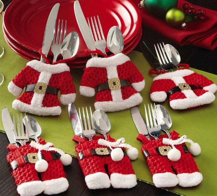 Set of silverware in Santa Claus outfits on a green tablecloth with red plates in the background.