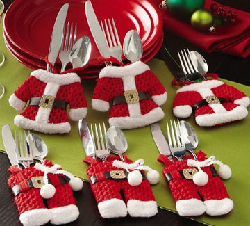 Set of silverware in Santa Claus outfits on a green tablecloth with red plates in the background.