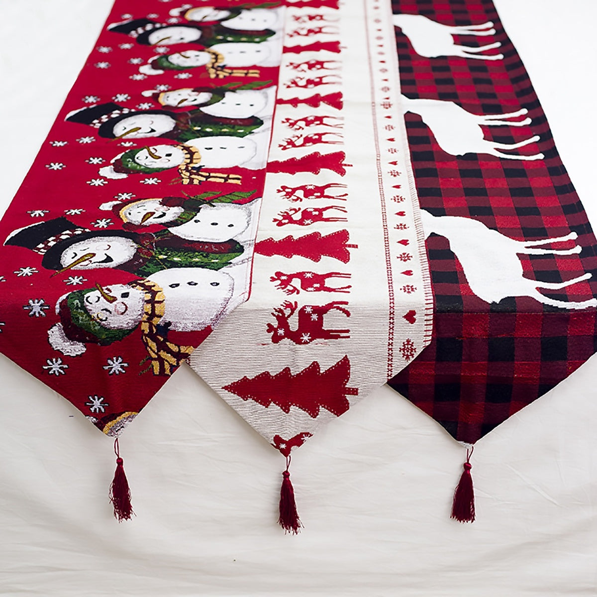 Christmas-themed table runner with snowmen, reindeer, and plaid patterns on a white surface.